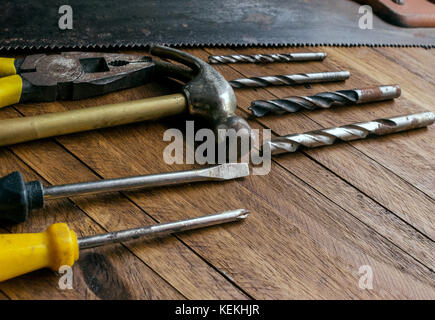 Rusty and old used carpentry and garage tools on a light brown wood background, showing varied tools,with metal pliers and saw,metal drill bits,hammer Stock Photo