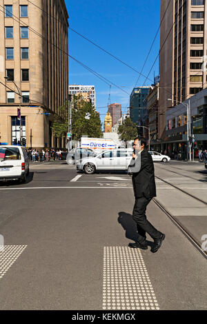 City worker talking on mobile phone while crossing street in Melbourne Victoria Australia. Stock Photo