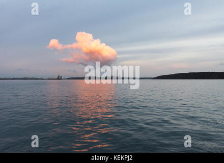 Evening sun on clouds over Pembrokeshire oil refinery seen from a yacht anchored at Dale Stock Photo