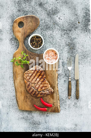 Grilled ribeye beef steak with herbs and spices on walnut cutting board over grunge grey background, top view Stock Photo