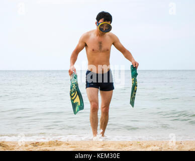 swimmer leaves the sea on the shore. In the hands of the flippers, on the head is a mask for diving. Accessories for diving. Beach vacation. Stock Photo