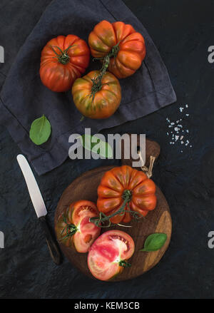 Fresh ripe hairloom tomatoes and basil leaves on rustic wooden board over black stone background., top view Stock Photo