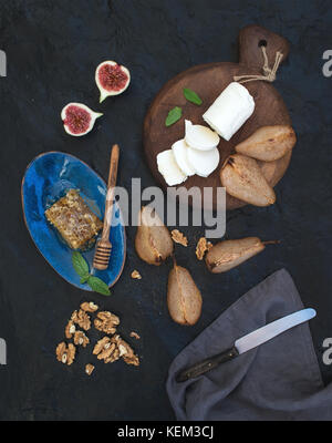 Appetizer set. Roasted pears, goat cheese on rustic dark wooden board, fig, honey and walnuts over black stone background, top view Stock Photo