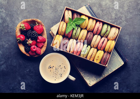 Colorful macaroons and berries on stone table. Sweet macarons and coffee cup. Top view. Retro toned Stock Photo