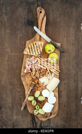 Wine appetizers set: cheese selection, honey, grapes, almonds, walnuts, bread sticks, figs on olive wood serving board over rustic background , top vi Stock Photo