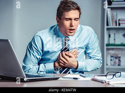 Office manager having heart attack. Photo of young man holding hand on painful chest in the workplace. Medical concept. Stock Photo