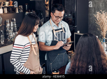 Asia Barista waiter take order from customer in coffee shop,Two cafe owner writing drink order at counter bar,Food and drink business concept,Service  Stock Photo