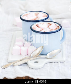 Seint Valentine's holiday greeting set. Hot chocolate and heart shaped marshmallows in old enamel mugs on white ceramic serving board  Stock Photo