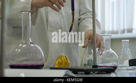 Lab technician doing experiment in lab. Male medical or scientific laboratory researcher performs tests with blue liquid. Scientist working with flasks in laboratory Stock Photo