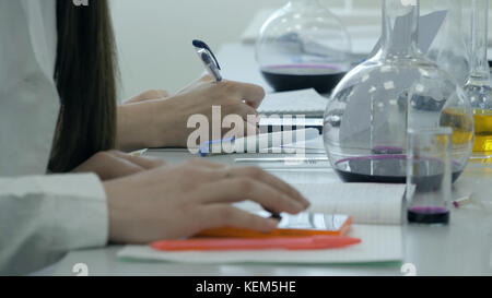 Students at work in the laboratory of chemistry take notes in a notebook. Female Pupil Using phone In Science Lesson. Young medical students write Stock Photo