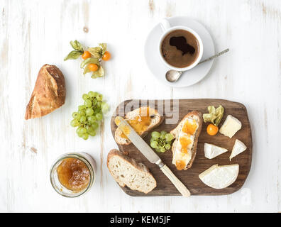 Breakfast set. Brie cheese and fig jam sandwiches with fresh grapes, ground cherries. Cup of coffee. Top view Stock Photo