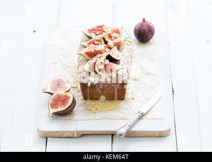 Loaf cake with figs, almond and white chocolate on wooden serving board over grunge background, selective focus. Stock Photo
