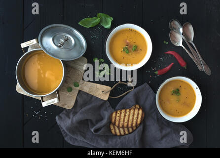 Red lentil soup with spices, herbs, bread in a rustic metal saucepan and bowls, over dark wood backdrop, top view Stock Photo