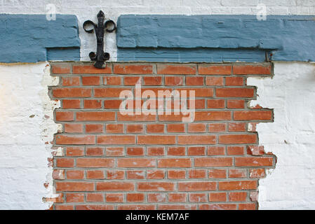Red brick wall with wrought-iron decoration, partly plastered with white and blue-grey plaster Stock Photo