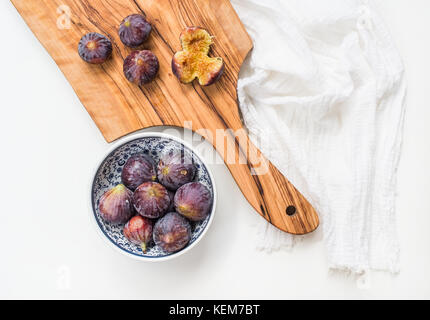 Fresh figs in blue patterned ceramic bowl and on olive wood board over white background Stock Photo
