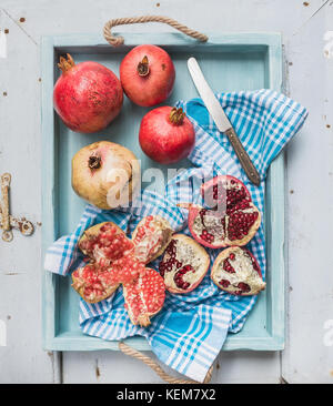 Red and white pomegranates with knife on kitchen towel in blue tray over light painted wooden backdrop Stock Photo