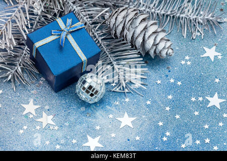 silver christmas tree branches with cones, decorations and blue gift box on blue background Stock Photo