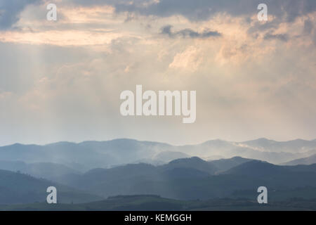 Various layers of hills and mountains with mist between them, with sun rays coming out through the clouds Stock Photo