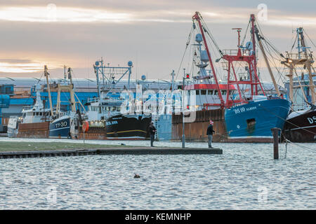 22nd October 2017; Shoreham Port, West Sussex, UK; two men fishing with rods within the port just after dawn. Fleet of trawlers berthed in background. Stock Photo
