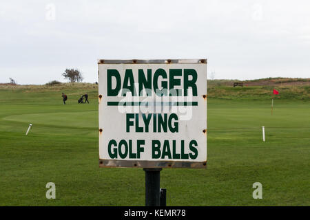 Golf course sign warning of flying golf balls with two golfers and a red flagged hole in the background with copy space Stock Photo