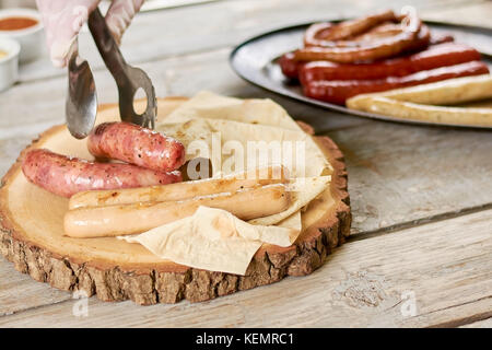 Chef putting grilled sausages on natural wood. Assorted sausages and lavash on wooden platter. Delicious european food. Stock Photo