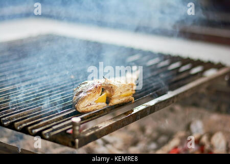 Fish with lemon grilling on grill. Preparing dorado fish on iron grill at restaurant. Seafood cooking at restaurant. Stock Photo