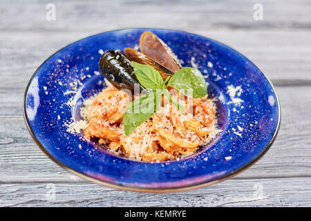 Pasta served with mussels and fresh basil. Delcious pasta with seafood and parmesan on blue porcelain plate. Stock Photo