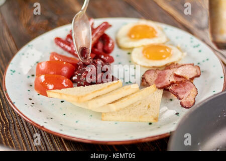 Full english breakfast on plate. Chef putting beans on plate with english breakfast. English breakfast in restaurant. Stock Photo