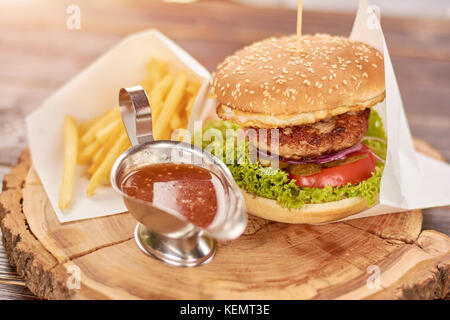 Appetizing burger with double meat. Delicious burger with french fries and sauce on wooden board. Tasty dinner in restaurant. Stock Photo