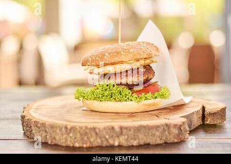 Appetizing cheeseburger on wood. Big humburger with cutlets, cheese, tomatoes, lettuce, onion, pickled cucumbers. Classic american food. Stock Photo