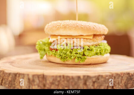 Delicious chicken burger with vegetables. Fresh appetizing cheesburger on natural wood. Classic american food. Stock Photo