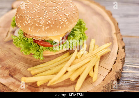 Fresh tasty burger and french fries. French fries and appetizing cheeseburger on natural wood. Classic american food. Stock Photo