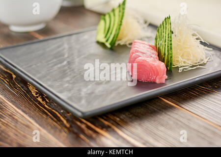 Tuna and cucumber on plate for sushi. Preparing of sashimi from tuna at professional kitchen. Ingredients for sushi on wooden table. Stock Photo