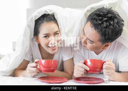 Young Asian Couples having breakfast on bed together in bedroom of contemporary house for modern lifestyle concept Stock Photo