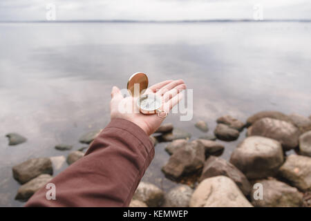 A traveler man holds a compass in his hand, standing on a stone beach Stock Photo