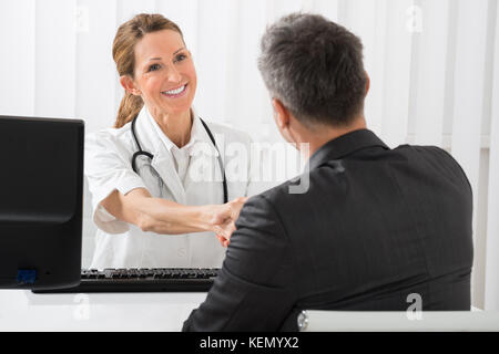 Happy Female Doctor Shaking Hands With Businessman In Hospital Stock Photo