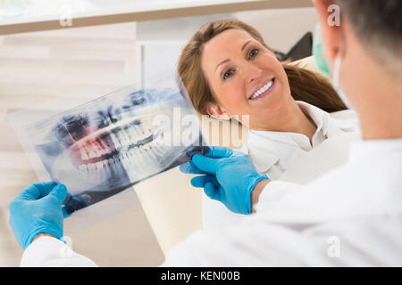 Dentist With Teeth X-ray In Front Of Happy Woman In Clinic Stock Photo