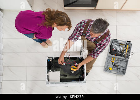 High Angle View Of Woman Looking At Technician Checking Washing Machine With Digital Multimeter Stock Photo