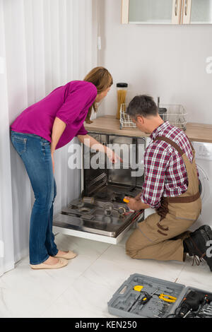 Woman Looking At Male Repairman Checking Dishwasher With Digital Multimeter Stock Photo