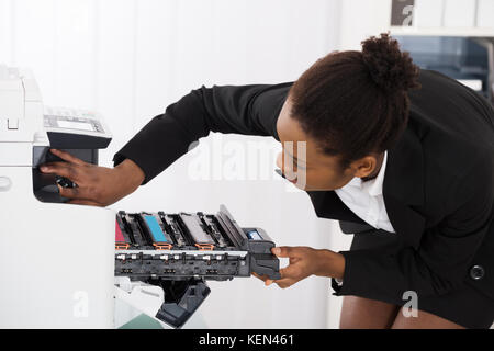 Young Businesswoman Fixing Photocopy Machine In Office Stock Photo
