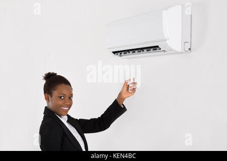 Young Happy Businesswoman Operating Air Conditioner With Remote Control In Office Stock Photo