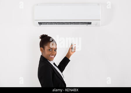 Young Happy Businesswoman Operating Air Conditioner With Remote Control In Office Stock Photo
