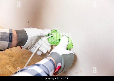 Hands of electrician installing socket in gypsum wall Stock Photo