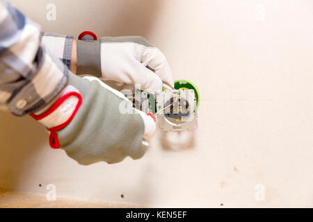 Hands of electrician installing socket in gypsum wall Stock Photo