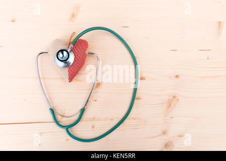 Stethoscope and red fabric heart lying on wooden table. Healthcare, cardiology and medical concept