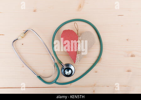 Stethoscope and red fabric heart lying on wooden table. Healthcare, cardiology and medical concept Stock Photo