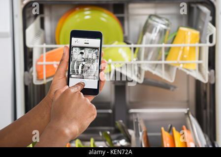 Close-up Of Person Hands Operating Dishwasher With Mobile Phone Stock Photo