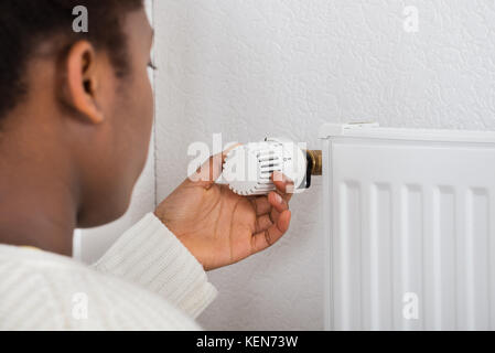 Woman Adjusting Temperature Of Radiator Using Thermostat Stock Photo