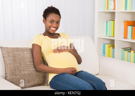 Happy Pregnant Woman Sitting On Sofa At Home Stock Photo