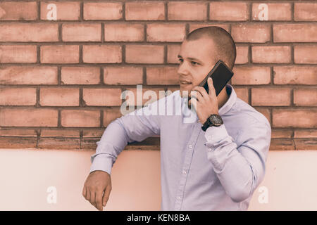 Handsome young man stands in front of a  old building and talks over a mobile phone. Stock Photo
